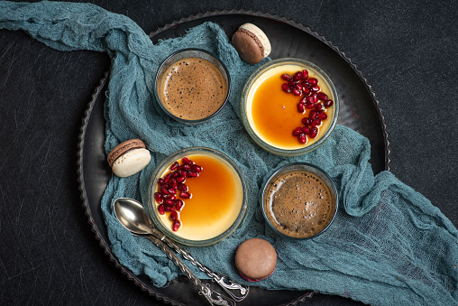 Creme brulee, colorful macaroons cookies and a cup of coffee. Traditional French dessert with vanilla cream in a glass bowl on a dark background