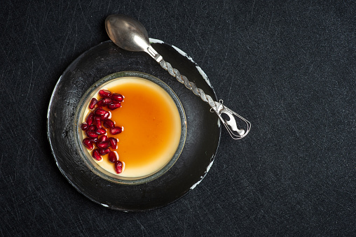 Cream brulee with pomegranate seeds. Traditional French vanilla cream dessert in a glass bowl on a black background
