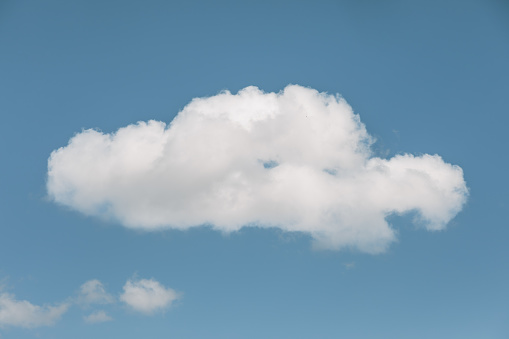 A solitary cumulus white cloud peacefully drifts through a clear blue sky with copy space area