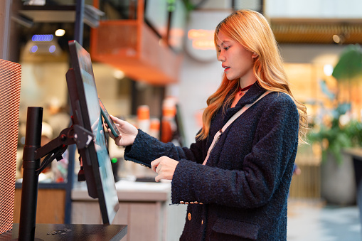 young Asian female using kiosk to order food