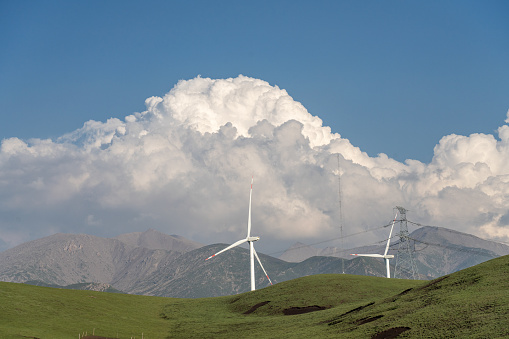 The wind turbine on the grassland with blue sky and white clouds descending the mountain