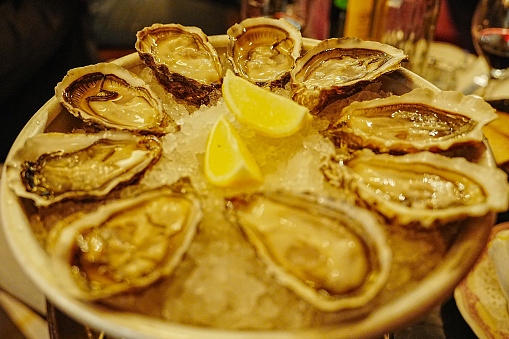 Woman eating fresh oysters with lemon close-up. Table with big plate of oysters and pink sparkling wine in a glass
