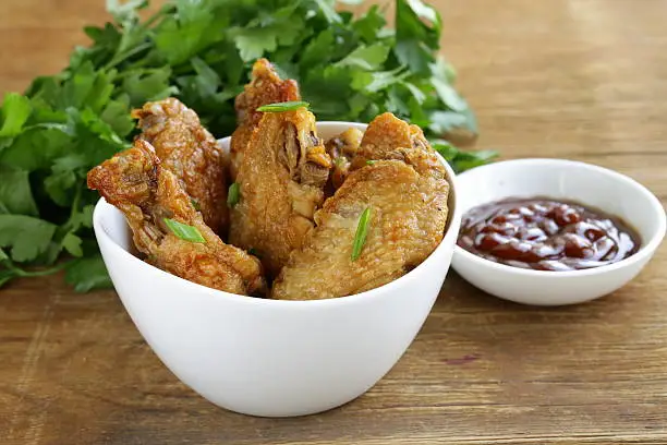 Fried chicken wings with hot  sauce in a white bowl