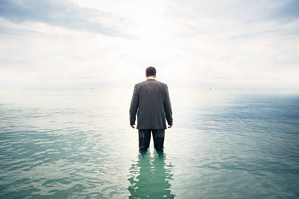 businessman knee-deep in water businessman is knee-deep in water walking in water stock pictures, royalty-free photos & images
