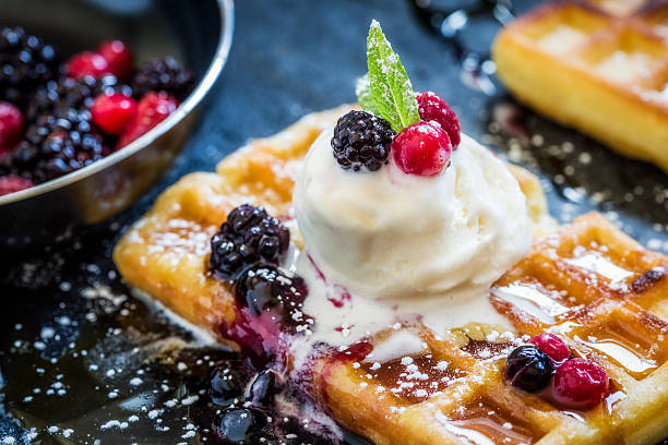A waffle with ice cream, dripping in syrup and berry sauce