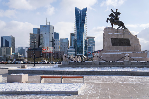Ulaanbaatar, Mongolia - November 8, 2023: An equestrian statue of Damdin Sükhbaatar is seen in front of buildings surrounding a snow-covered Sukhbaatar Square in central Ulaanbaatar.