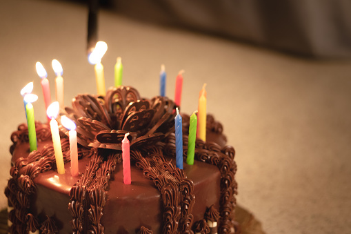 A chocolate birthday cake with colorful candles being blown out