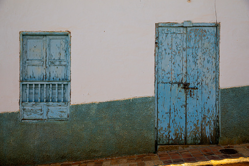 A rustic and weathered doorway and shuttered doorway in the town of  lovely colonial town of Barichara, which has white washed houses, cobble stoned streets and red tiled roofs. The town was declared a national monument in 1978.