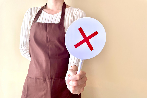 A young woman in an apron holding a NG sign placard