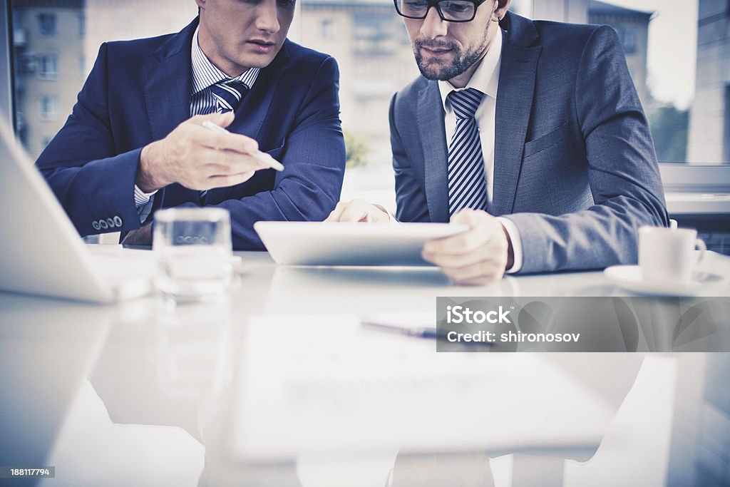 Two businessmen having a discussion and using tablet Image of two young businessmen discussing document in touchpad at meeting Adult Stock Photo