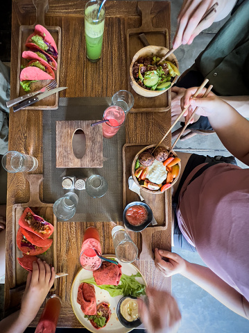 Multiracial, 2 generation extended family eating tacos, burritos, tempeh falafels and salad at a vegan cafe with friends and family.  Bali, Indonesia.