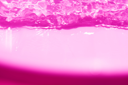 Purple water splashes on the surface ripple blur. Defocus blurred transparent pink colored clear calm water surface texture with splash and bubble. Water waves with shining pattern texture background.