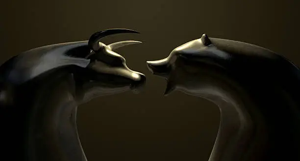 A closeup of two bronze castings depicting a stylized bull and a bear in contrasting light representing a financial market trends on an isolated dark background