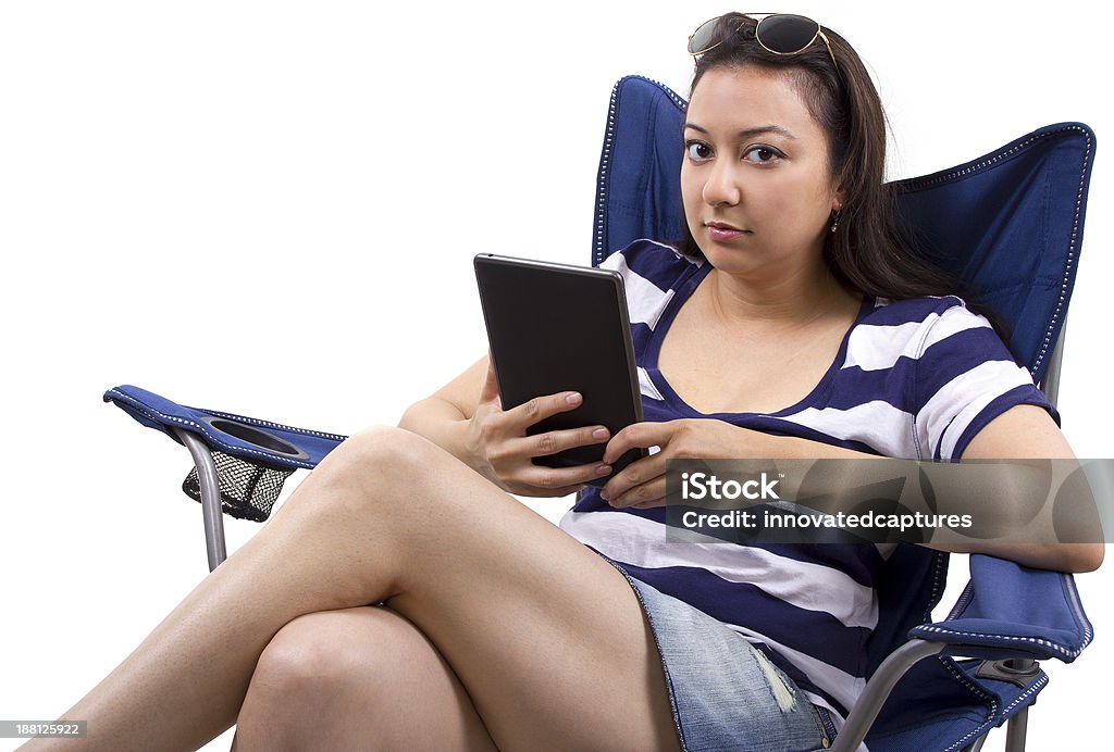Woman on a Lawn Chair Reading on a Tablet young female with tablet and sitting on a beach chair Chair Stock Photo