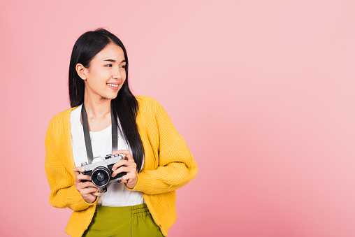 Attractive energetic happy Asian portrait beautiful cute young woman teen excited smiling holding vintage photo camera, studio shot isolated on pink background, traveler female photographer