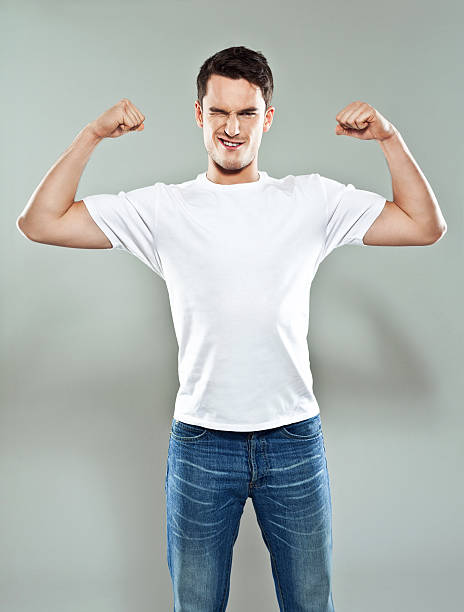 Strong man Portrait of young man wearing white t-shirt flexing her muscles and winking. Studio shot, gray background. young man wink stock pictures, royalty-free photos & images