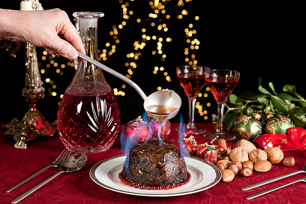 Flames on the christmas pudding Hand serving burning brandy over a christmas or plum pudding christmas pudding stock pictures, royalty-free photos & images