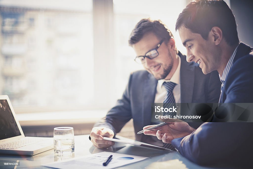 Two businessmen talking while looking at notes Image of two young businessmen using touchpad at meeting Business Meeting Stock Photo