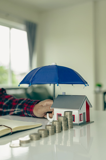 Blue umbrella covering a house model on a wooden table Property insurance, mortgage insurance concept Insurance is risk control in the real estate business.