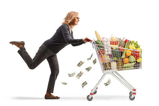 Woman running with a shopping cart and money falling from the cart isolated on white background