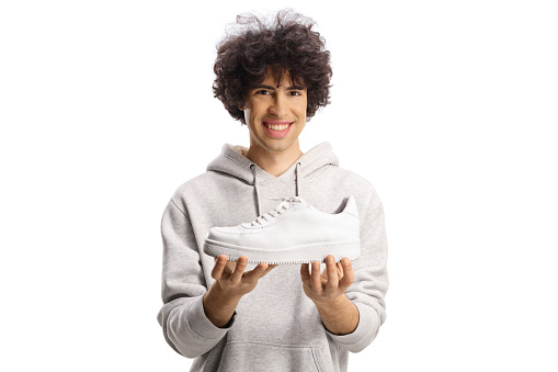 Happy young man holding a trendy white sneaker isolated on white background