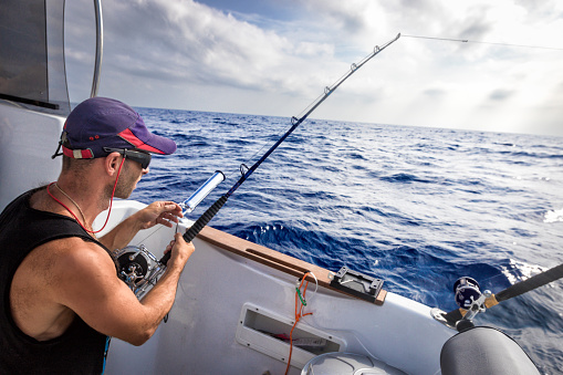The young man in a baseball cap onboard the vessel in the course of fishing against the background of the blue sea.
