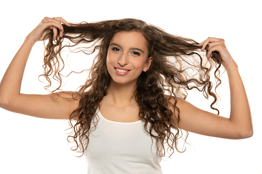 Young happy woman showing heer long wavy hair on a white studio background