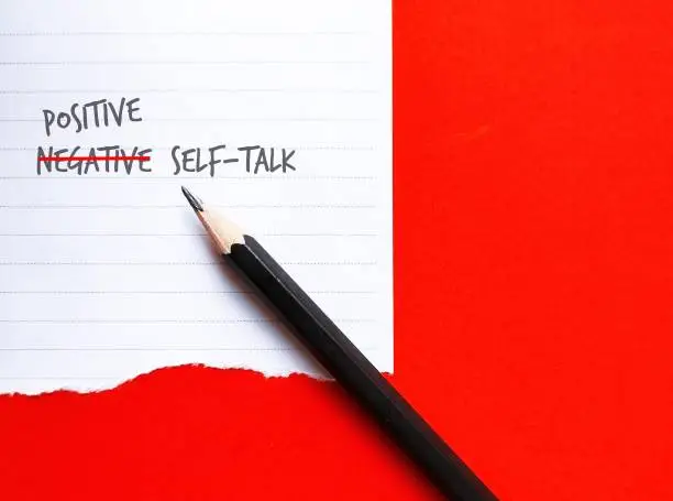 Pencil on red background with note NEGATIVE SELF-TALK changed to POSITIVE, concept of overcome negativity inner voice critics which impact confidence, change them to positive optimistic ones