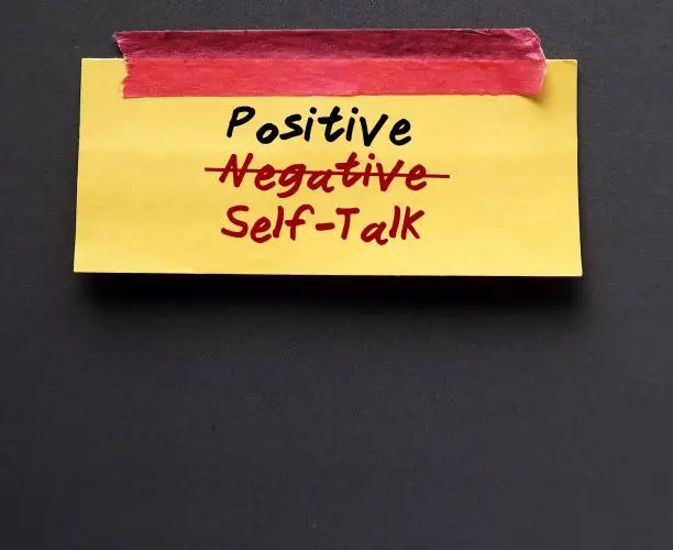 Yellow note stick on gray copy space background with handwritten text NEGATIVE SELF-TALK corrected to POSITIVE, means to have self awareness, beware negative inner thoughts and change to positive ones to boost self esteem