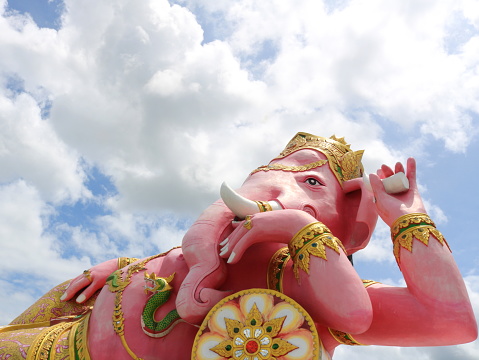 Bright pink painted Ganesha concrete statue recline posture and clouds on sky background, Thailand.