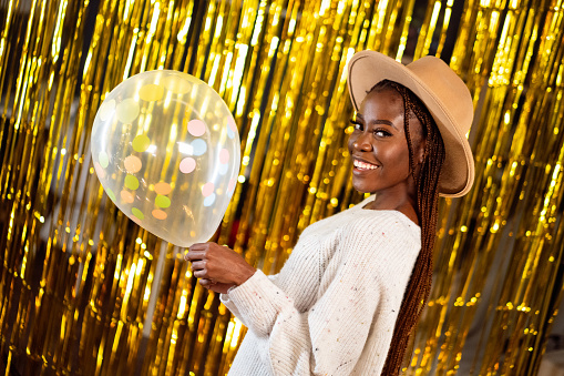 Party portrait of a beautiful African ethnicity woman posing against the gold fringe curtains.