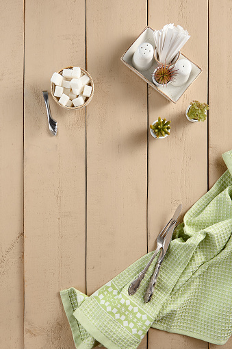 Rustic wooden table setting in a cafÃ©, featuring sugar cubes, napkins, and cutlery from a top-down perspective.
