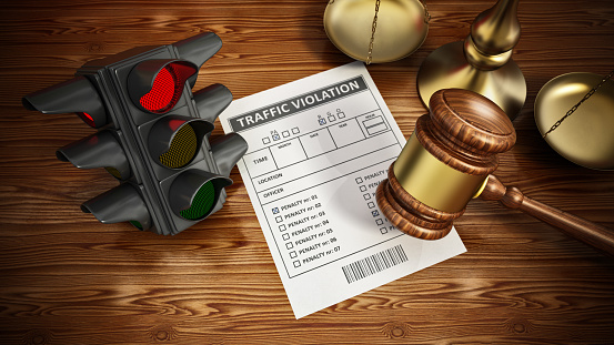 Traffic ticket under wooden gavel. Red traffic light and balanced scale in the background....