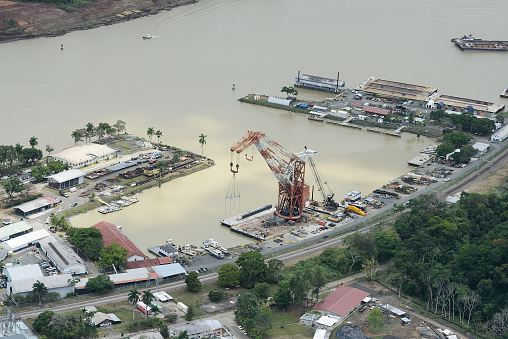 Aerial view of an industrial area along a waterway in Panama, featuring cranes, vessels, and commercial buildings