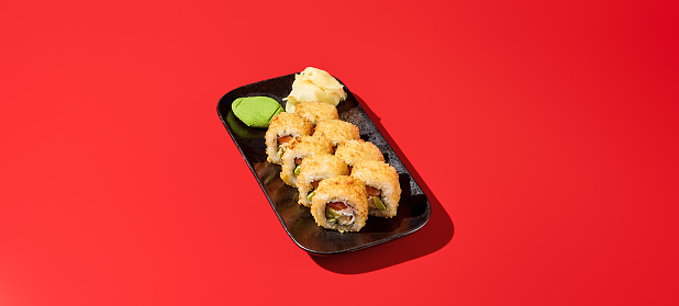 Hot tempura sushi roll with salmon and avocado, vividly displayed on a black plate against a bold red backdrop. Perfect for a banner with copy space.