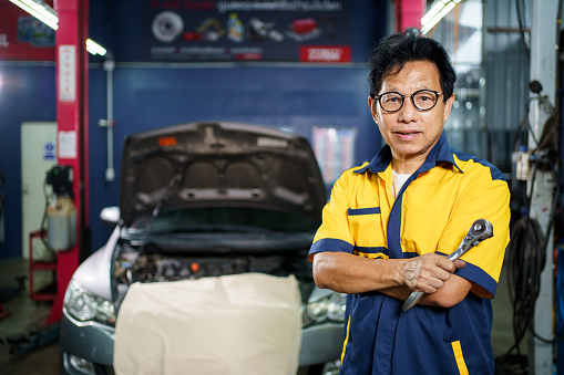 Professional Asian vehicle technician posing for photography in garage. Handsome Asian repairman or technician examining a vehicle in garage.