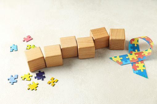 Ribbon with colorful puzzle pieces and wooden cubes on light background. World autism day concept