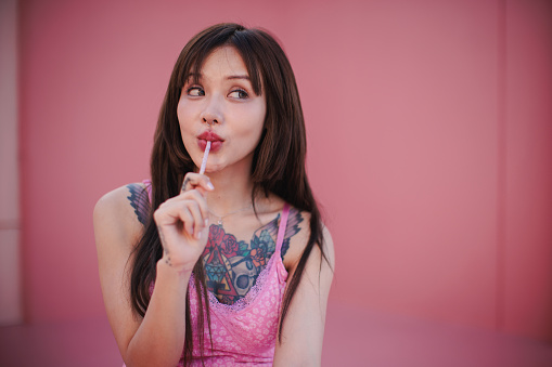 An attractive, smiling woman is eating candies against a soft, pink backdrop.