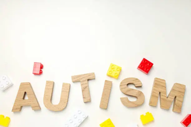 The word "autism" in wooden letters on a light background with legos, place for text. World autism day concept