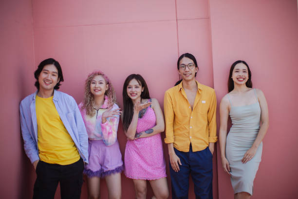 Friends smiling directly at the camera against a soft pastel pink background.