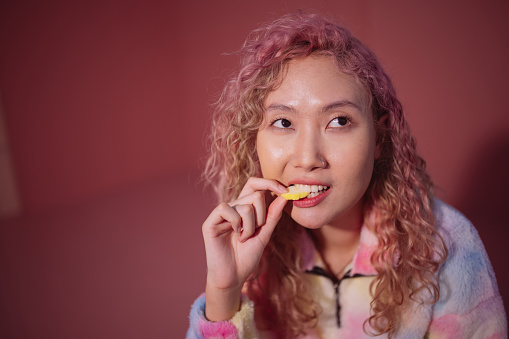 A woman bites into a gummy candy against a pink background.