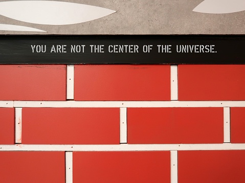 Brown brick wall with text inscription YOU ARE NOT THE CENTER OF THE UNIVERSE, to remind we are not focus of everyone attention, we are much more focus of ourselves mistakes and flaws