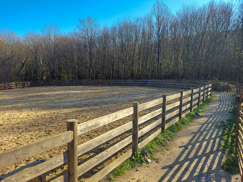 Half-open gate of the sandy racing track surrounded by fences for horses