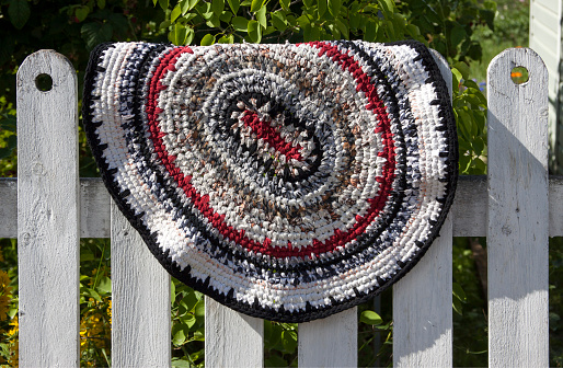 Handmade rug in red, black and white in rustic style on a white wooden fence