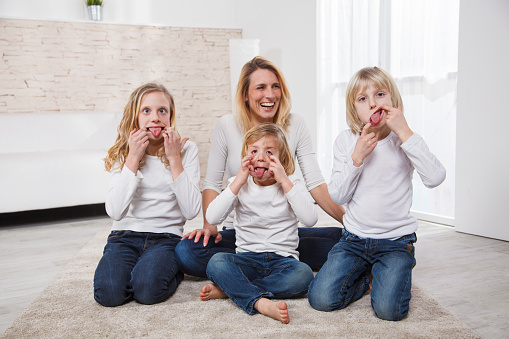 Cross-eyed girl and two boys making faces. Mother having fun with her children. Siblings in jeans and white tshirts. Family time.