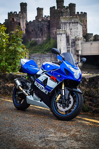 conwy, United Kingdom – December 01, 2023: A close-up of a Suzuki motorcycle parked against a backdrop of Conwy castle in Wales