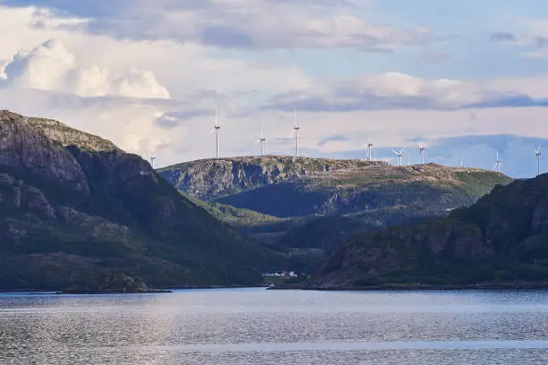 Windmills electric powerplants on the top of the mountain ridge above the fjord in Norway. Green renewable resource of electric energy, most important part of responsible sustainability in the future.