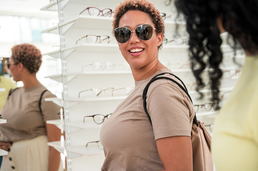 Mature Hispanic woman with Black female friend at boutique, analyzing eyewear options, stylish accessory shopping, companionship, diverse consumers, summer fashion trends.