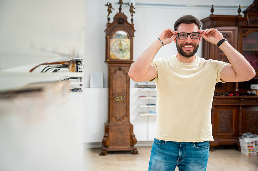 A Hispanic young adult male browses through an exquisite collection of eyeglass frames, reflecting his taste in a mirror at an upscale optical boutique.