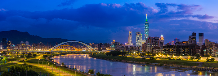 Panoramic view across the Keelung River to the glittering high-rise cityscape, skyscrapers in the heart of Taiwan’s vibrant capital city at dusk.